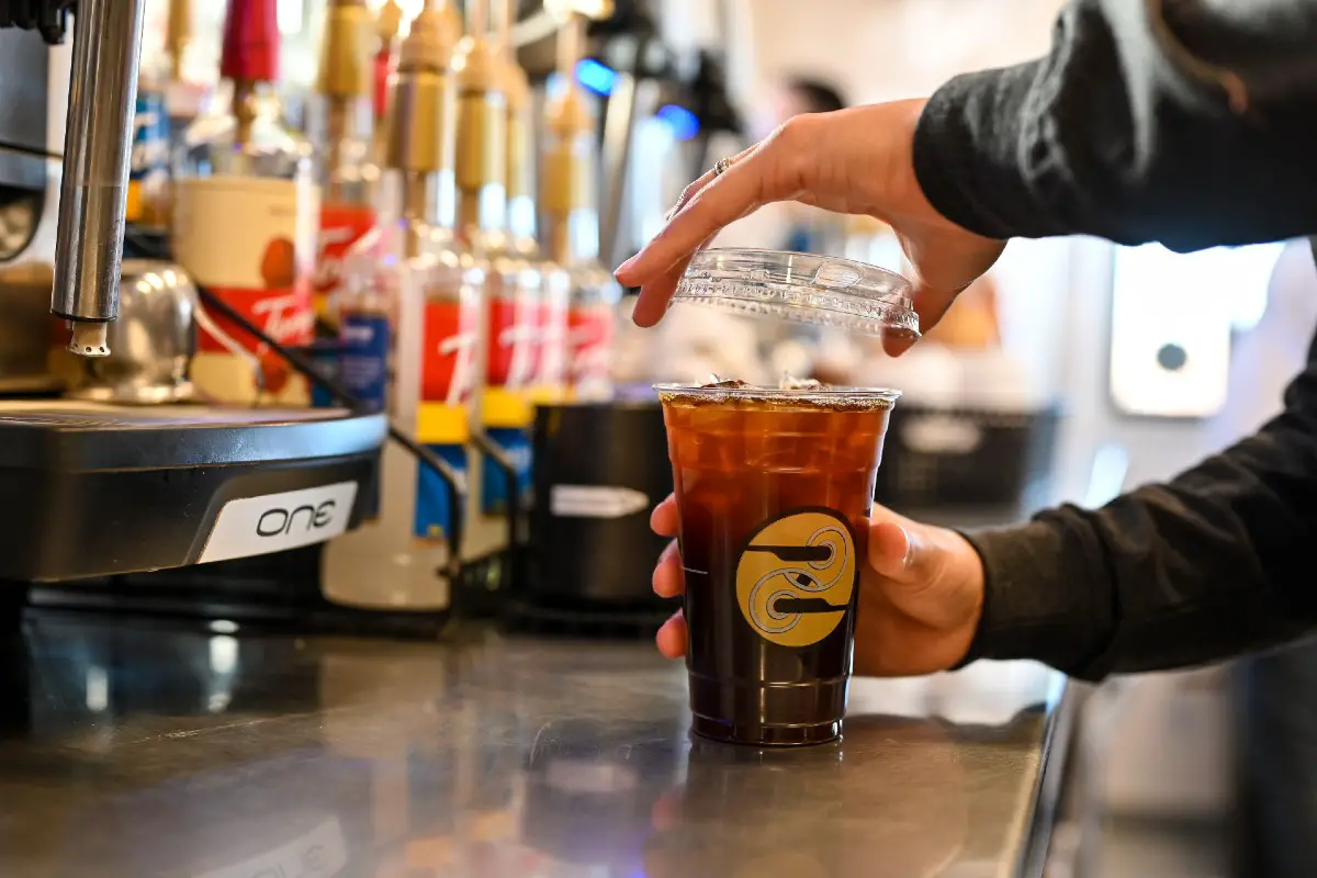 A Ziggi's Coffee barista putting the top of an iced coffee behind the service bar.